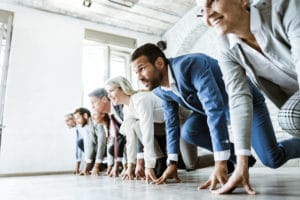 Large group of business people on a starting line ready for sports race in the office. Focus is on man in blue suit. Copy space.