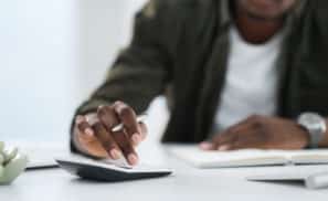 Shot of a young man using a calculator at work