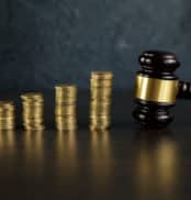 Close-up Of A Judge's Hand Holding Gavel Over Stacked Golden Coins